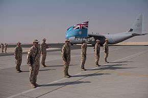 Personnel in camouflage uniforms with RAAF flag lined up in front of four-engined military cargo plane in grey livery