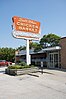 A large orange sign on a white pole next to a one-story building