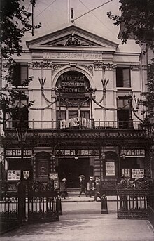 Photo noir et blanc. Vue de face. Au premier plan, entrée et feuillages de Leicester Square.