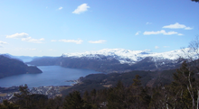 Foto von einem Berg auf einen Fjord hinab, an dessen inneren Ende eine Siedlung liegt