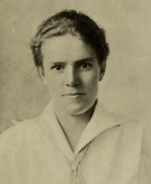 A young white woman, with short wavy hair, wearing a collared white blouse; she is looking directly at the camera