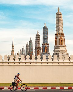 A man wearing face mask cycling outside the wall of the Grand Palace, Bangkok Photographer: Kriengsak Jirasirirojanakorn