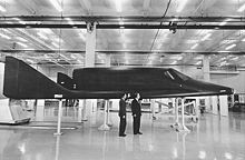 Men stand next to a sleek, black spaceplane.