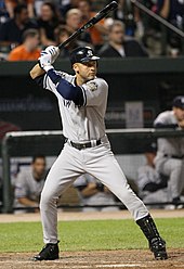 A right-handed African American baseball batter. He is wearing a grey uniform with blue sleeves underneath, and is in a batting stance.