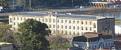 A very long white building sits on a small body of water, partially obscured by trees.