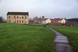 A greenspace, bisected by a footpath, with buildings in the middle and far distance