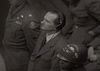 Lanz is seen at the Nuremberg Trials. He is heavily guarded and is wearing headphones.