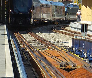 Ein aus Interlaken kommender GPX-Zug am Bahnsteig 6 in Zweisimmen. Der Lok-Wechsel ist beendet: hinten die den Zug durch eine Umspuranlage und nach Montreux weiter schiebende MOB-Lok. An den Seiten der Anlage die hochgeklappten blauen Rampen.