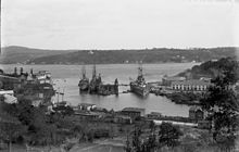 A large warship is tied to the dock in a narrow channel of water.