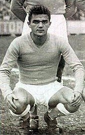 Photographie en noir et blanc d'un homme accroupi vu de face en tenue de footballeur avant un match.