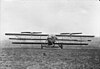 A bizarre-looking triplane flying machine with two rotors above the wings faces the camera.