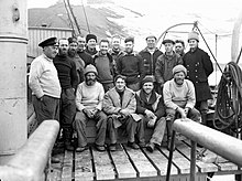 Photo noir et blanc, portrait d'un groupe de seize hommes chaudement vêtus sur le pont d'un bateau.