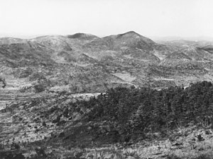 A series of ridgelines and steep hills in the distance, with Maryang-san on the right. In the foreground is a heavily vegetated knoll, with a valley in the intervening ground.