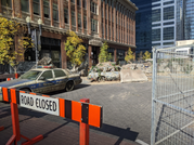 A street with dirty, damaged cars and broken concrete, behind an orange and black "Road Closed" sign