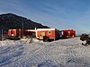 Red, flat, one-story building sitting on snow with a dirt hill in the background