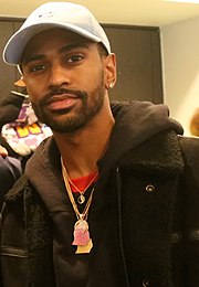 A black bearded man wearing a white cap and dark shirt poses for the camera