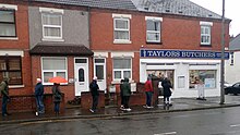 A line of people waiting on the sidewalk of a street, each standing at least 6 feet apart