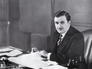 Photographie noir et blanc d'un homme assis à un bureau.