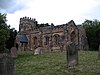 A stone church seen from the southeast, with both the west tower and the south aisle battlemented