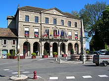 Photographie montrant un bâtiment au centre d'une place arborant à ses fenêtres différents drapeaux dont le drapeau français