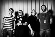 Magnapop posing in a black-and-white photograph in front of a striped wall.