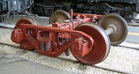 This Bettendorf-style freight car truck uses journal bearings in journal boxes that are integral parts of the side frames. The center pin can be seen pointing up from the bolster. It has coil springs.