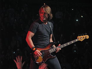 A fman with long blond hair playing a bass guitar