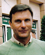 An out-of-focus portrait shot of a dark-haired man in a lime-green v-neck sweater