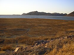 A photo of a dry lakebed with some ruined foundations