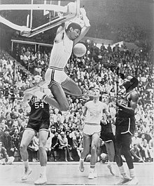 Lew Alcindor, suspendu au panier, sous les yeux d'adversaires et de coéquipiers.