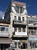 A narrow, four-story building with a large sundial and two clocks at the top