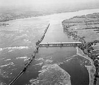 Photographie noir et blanc d'une vue aérienne sur un cours d'eau avec un barrage..