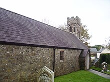 Photo d'un bâtiment allongé aux murs de pierre grise, avec une seule petite fenêtre, et au toit en ardoises. Une petite tour carrée crénelée se dresse du côté droit.