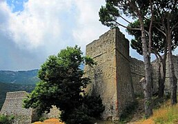Imposantes fortifications en bon état avec muraille et tours dans un environnement méditerranéen (pins maritimes, herbes sèches).