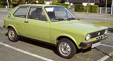 Front-three-quarter view of a small three-door car with steel wheels and no passenger-side door mirror.