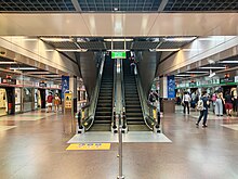 The lower platform level of the station, with escalators leading up to the concourse and the other platform.