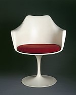 Photographie d’une chaise à piédestal au dossier blanc et coussin d’assise rouge.