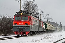 Photographie de devant d'un train de marchandise roulant sur des rails dans un paysage enneigé, avec des arbres autour des deux voies.