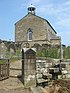 A small stone church standing in a churchyard on top of a hill. On the near gable is a bell-cupola.