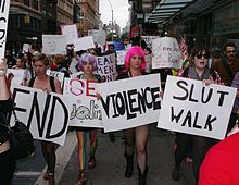 A group of people walk in a demonstration (a «SlutWalk») in New York City; many of them carry signs with slogans relating to and condemning sexual assault and discussing public perceptions thereof