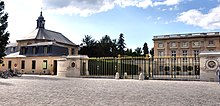 Photographie depuis la place avec la grille d'entrée et le château au fond.