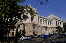 façade néo-classique alternant symétriquement des arcades droites et des travées cintrées sur trois niveaux : les deux premiers présentent une maçonnerie à bossages gris pâle, le troisième une façade enduite de blanc