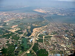 An aerial view of Jimei District (foreground and center), connected by numerous bridges with Xiamen Island's هولای (in the background right, including فرودگاه بین‌المللی زیامن گائوچی).