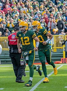 Aaron Rodgers, Jordan Love and another Packers player jogging on a football field in their uniforms during a game
