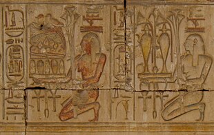 Relief showing two kneeling people carrying trays piled with plants, jars of liquid, and food