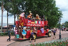 A red turn-of-the-20th-century-style double-decker bus with costumed characters onboard