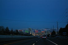 Dusk view of a freeway descending into a neon lit cityscape.