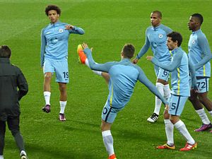 Three football players in blue suits warming up on a green pitch