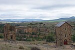 Two stone buildings, one partially ruined, with an open-pit mine in the background