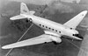 A twin-nacelled, low-wing aircraft without engines, bearing U.S. Army Air Forces insignia, in towed flight over fields